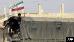 شام کے مشرقی علاقے میں ایک بچہ ایران کے پرچم کے ساتھ ایک فوجی ٹرک پر سوار ہے۔ فائل فوٹو